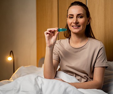 Young woman holding sleep appliance in bed 